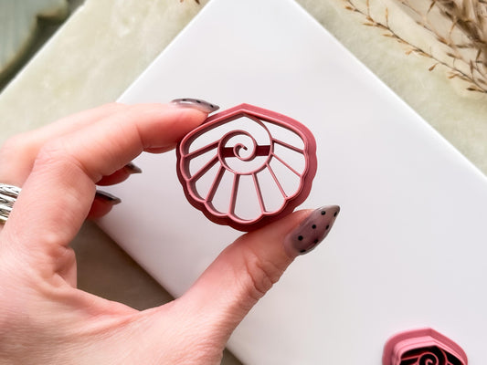 Large clam shell shaped clay cutter being held in the air. The image shows the stamp imprint details clearly .