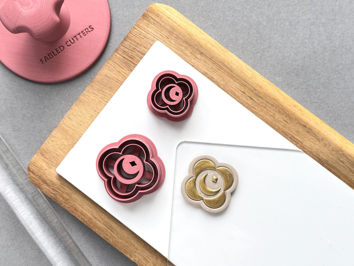 Crescent moon and star polymer clay cutters in two sizes, featuring a crescent moon centred within a decorative flower-shaped frame, displayed beside a matching finished clay embellishment in gold.