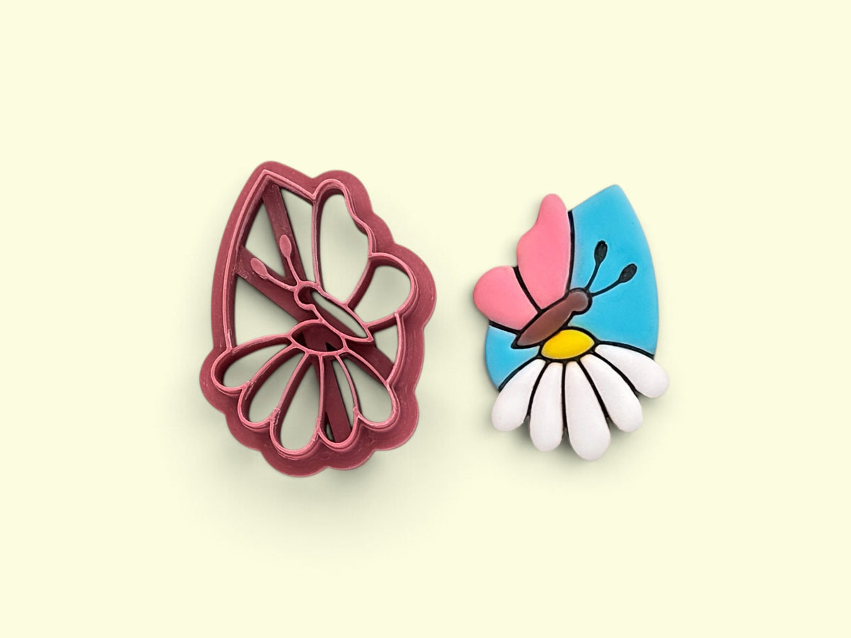 A tear-drop shaped clay cutter in pink plastic shown next to a colorful butterfly-shaped earring cut out on a pale yellow background.
