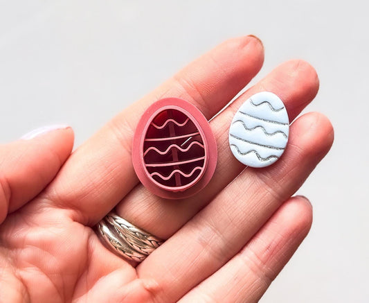Wavy line easter egg polymer clay cutter in hand with cut out clay decorated with silver ink