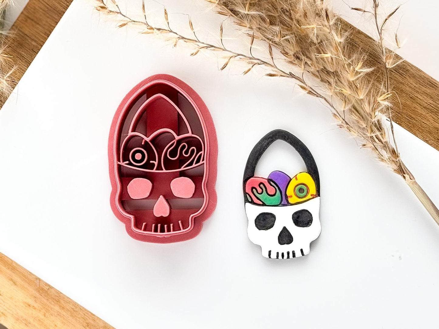 Gothic easter themed clay cutter with skull shaped basket and spooky easter eggs. Cutter is in pink on a white tile with a cut out clay earring next to it