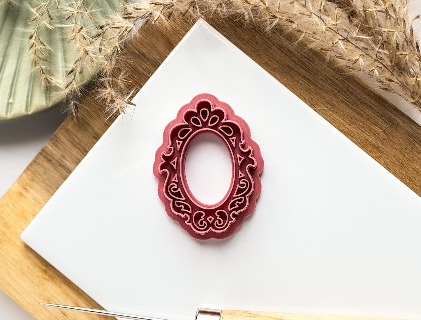Dark pink vintage frame shaped polymer clay cutter with stamp filligree details on a white background.