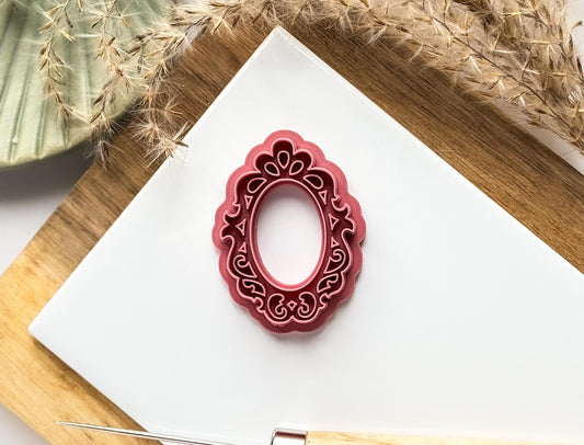 Dark pink vintage frame shaped polymer clay cutter with stamp filligree details on a white background.