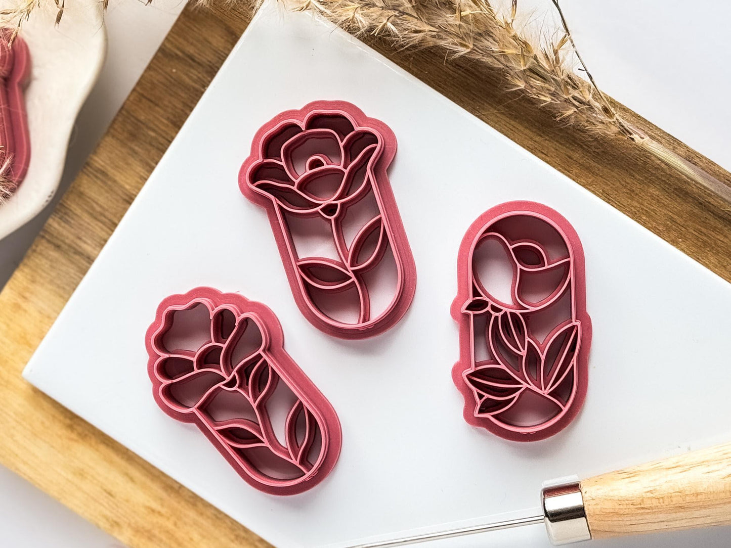 Polymer clay cutters in dark pink material in the shape of floral stained glass windows. Iris shaped cutter, peony shaped cutter and generic flower shaped cutter