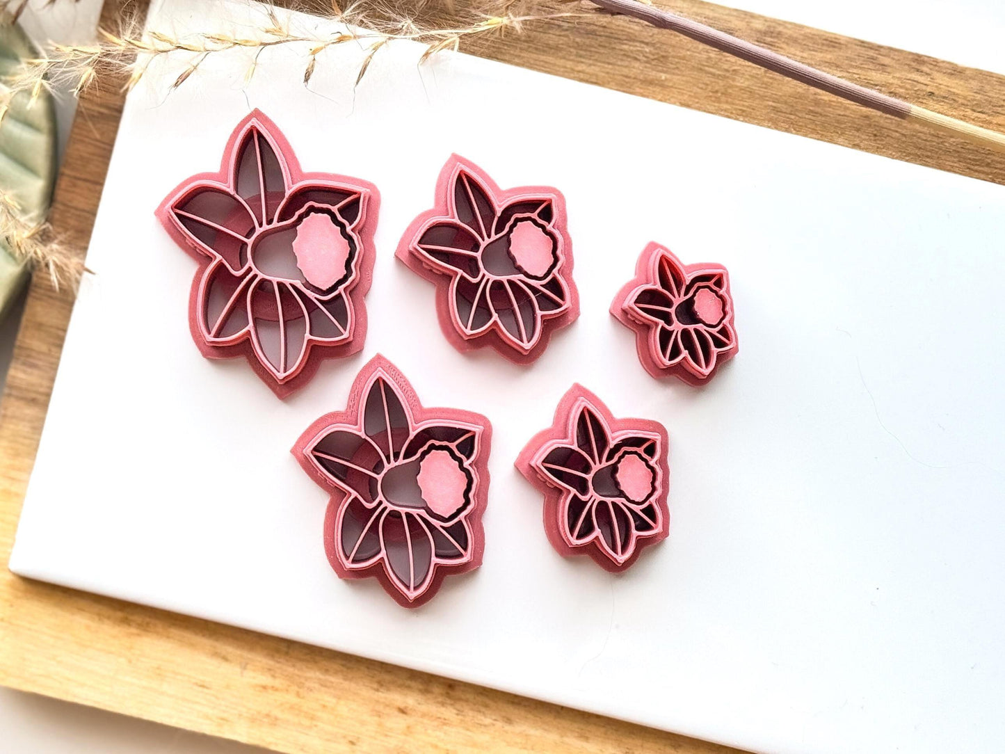 group of daffodil cutters for clay and silver clay. dark pink in colour on a white baking tile