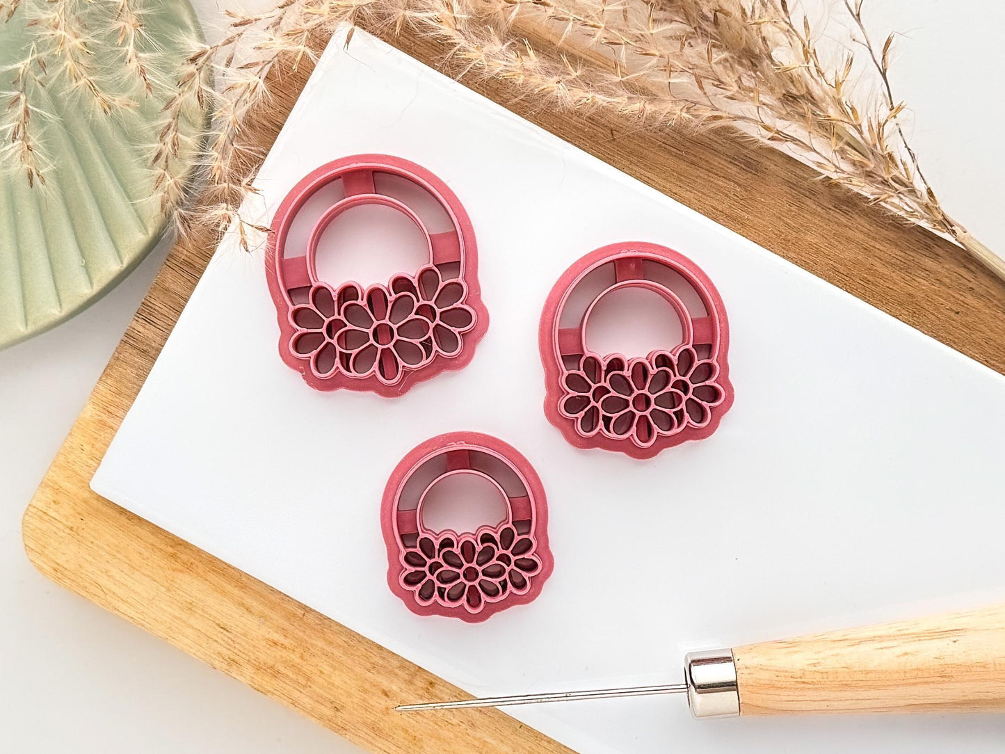 three sizes of daisy ring shaped clay cutter on a white clay baking tile sorrounded by clay tools, dried flowers and decorations.
