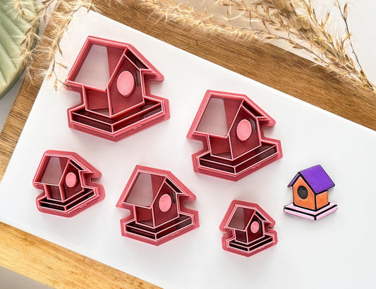 Group of dark pink bird house clay cutters and polymer clay cut out sample on a white tile