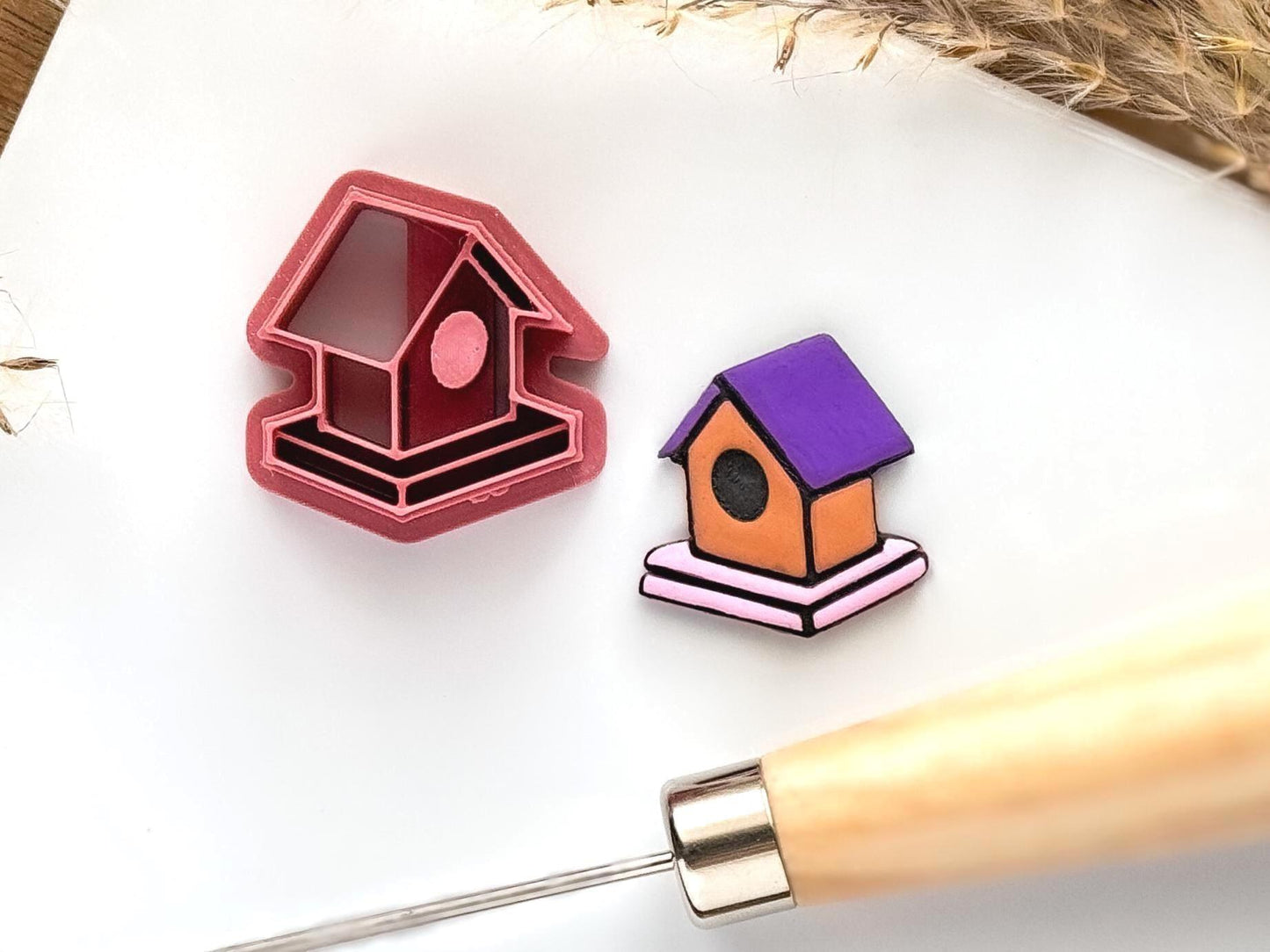 birdhouse table polymer clay cutter in dark pink next to a purple and brown clay bird house sample.