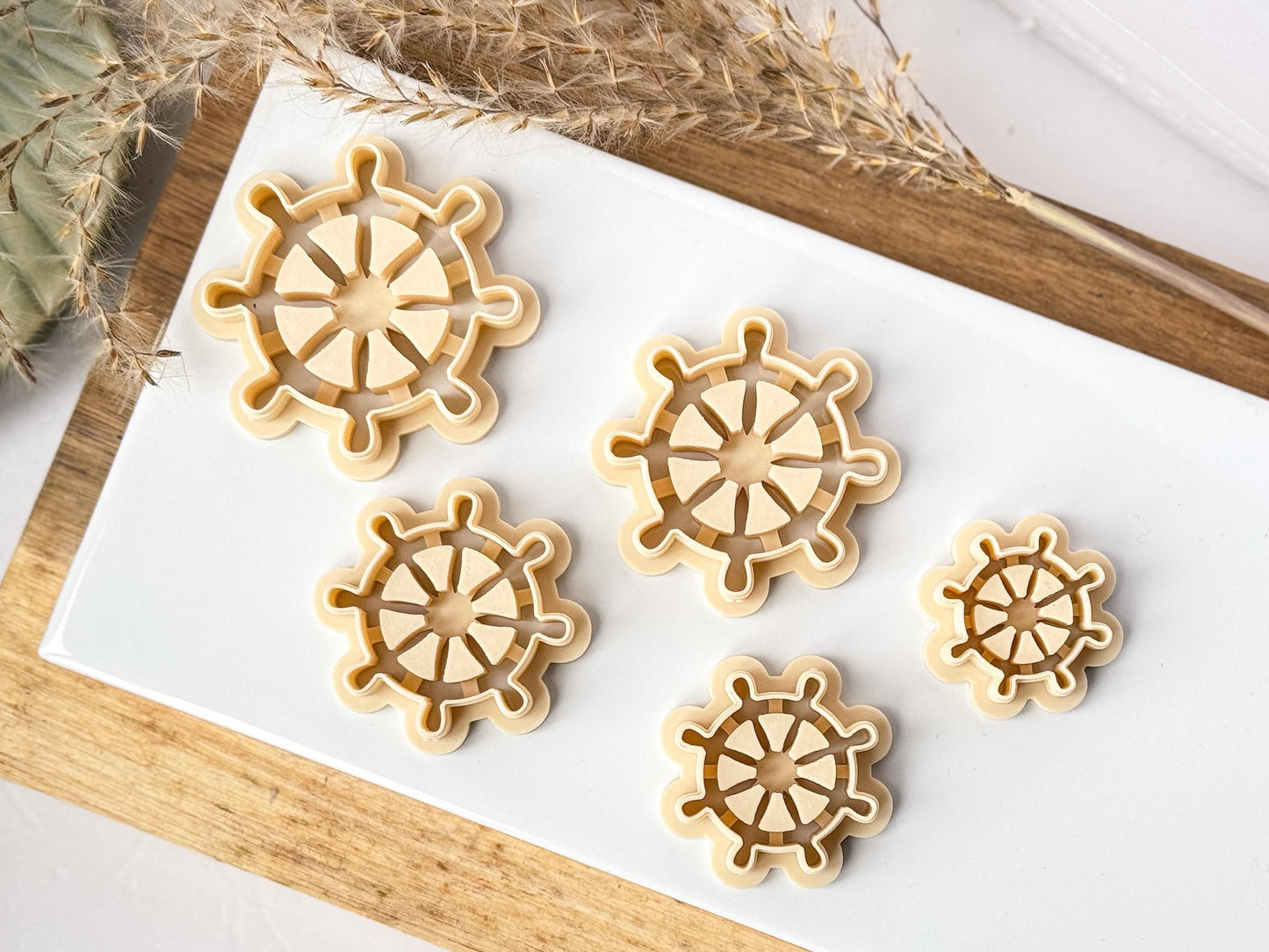Fove sizes of ships helm or wheel polymer clay cutters on a baking tile
