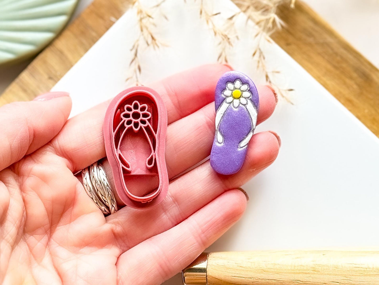 Summer sandle clay cutter with cut out shape showing straps and flower details being held in a hand for scale