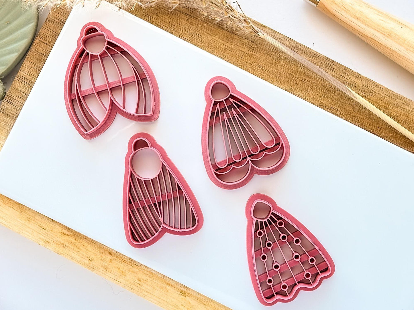 4 large moth clay cutters in dark pink on a white tile showing detailed imprint lines