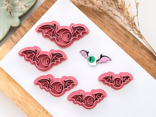 Various sizes of winged eyeball shape polymer clay cutter on white tile background