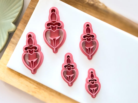 Various sizes of daggered heart silver clay cutter on a white tile