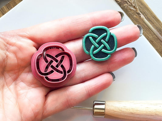 celtic knot shaped polymer clay cutter and black and green sample clay piece being held in a hand for scale.