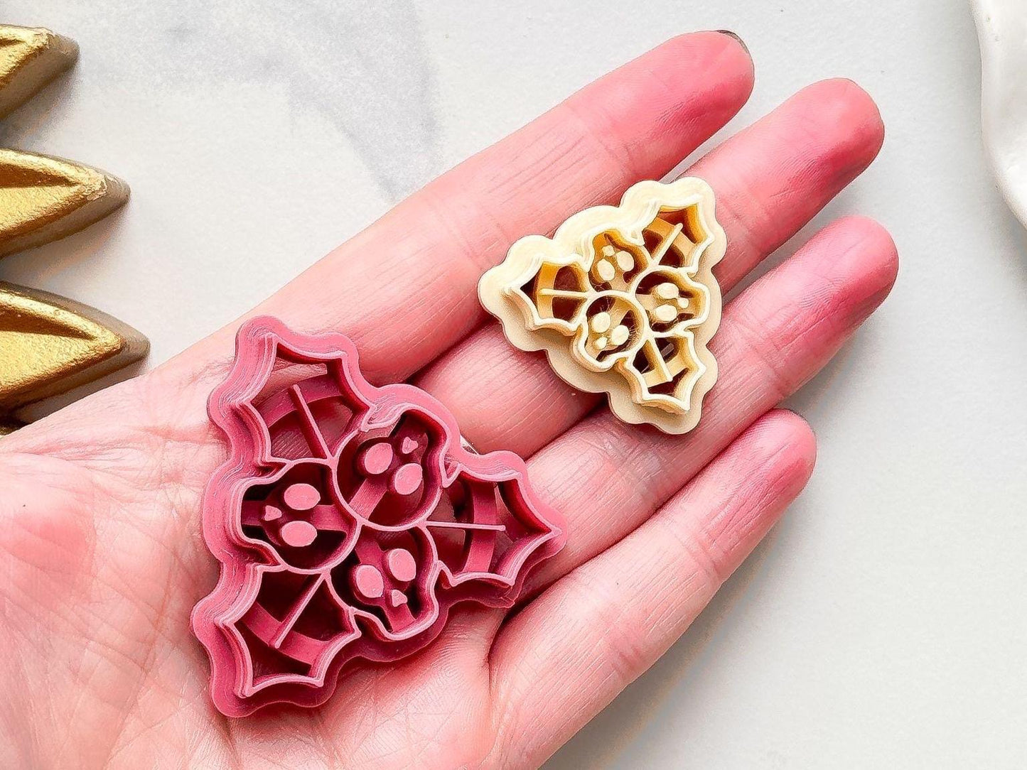 pink and beige holly cutters with three skull shaped berries in the middle being held in a hand.
