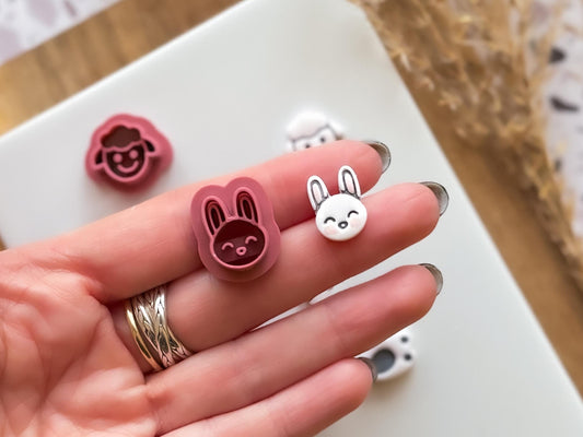mini rabbit face clay cutter and polymer clay cut out in a hand for scale. The cutter and cut out rest on 2 fingers.