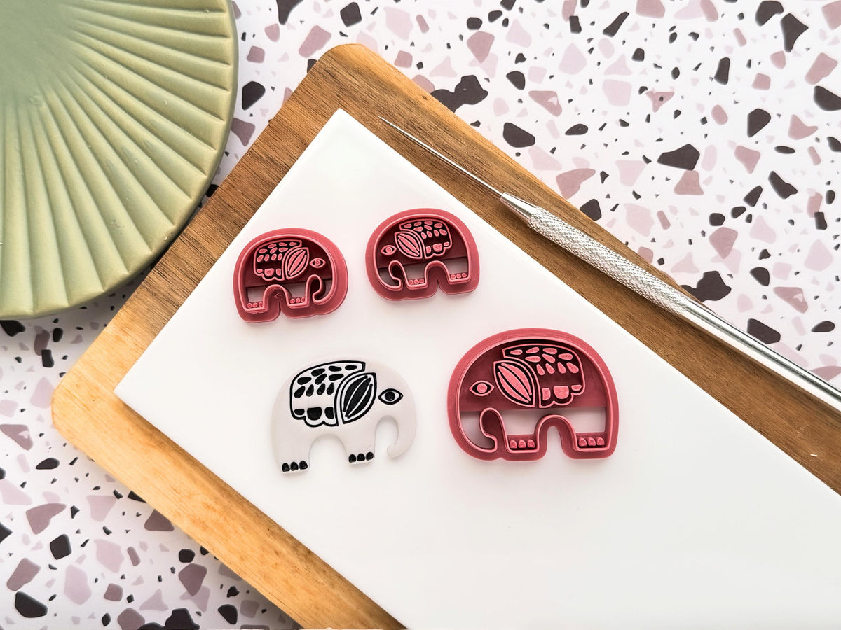 Boho style Elephant polymer clay cutters in a small mirrored pair and single large size. The elephants have a folk style stamping detail consisting of tribal-like dots and dashes. Next to the cutters is a grey polymer clay cut out sample.