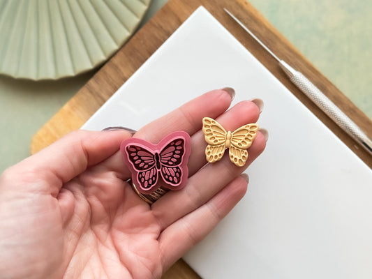 Monarch butterfly polymer clay cutter being held in a hand with a clay sample cut out showing embossed details.