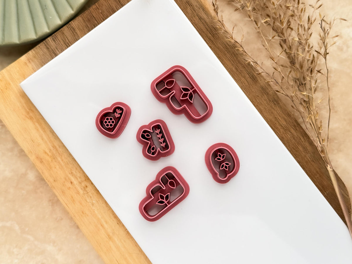 Floral boho alphabet clay cutters for polymer clay earring making in various sizes on a white tile.