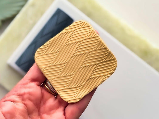 Beige polymer clay square ith geometric stripe pattern being held in a hand