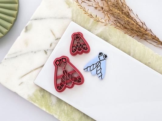 Two simple moth-shaped polymer clay cutters with detailed stamp pattern alongside a blue clay impression. UK-made crafting tools for polymer clay, fondant, jewellery making and creative craft projects.