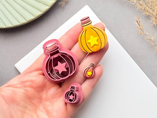 Potion bottle polymer clay cutter with star-shaped centre, held in a hand beside matching finished clay pieces in different sizes.