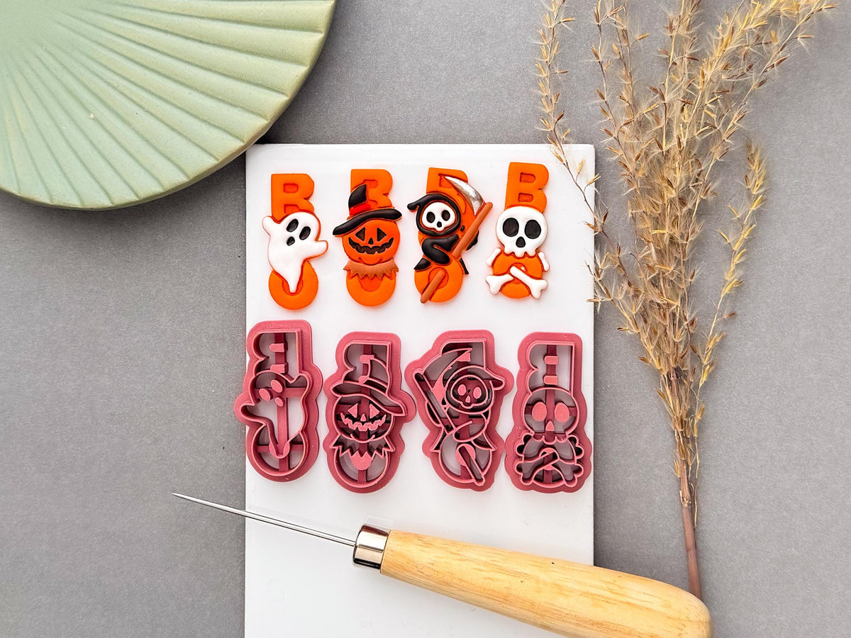 Halloween-themed 'boo' word clay cutters featuring ghost, pumpkin, skull and spooky character designs, with four detailed red cutters displayed alongside colourful Halloween clay shapes on a white work surface. Includes seasonal spooky craft designs for Halloween jewellery making and polymer clay projects.
