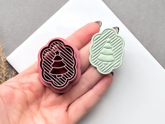 Pink polymer clay cutter shaped like a scalloped Christmas tree with diagonal striped detail and a small star at the top, shown beside a pale green finished clay tree held in a hand.