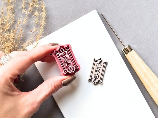 Rectangle frame clay cutter featuring three eyeball details arranged vertically within an ornate rectangular border, shown held in a hand beside a matching finished cream polymer clay cut-out. Pink 3D-printed cutter shown close-up to highlight the detailed stamp design.