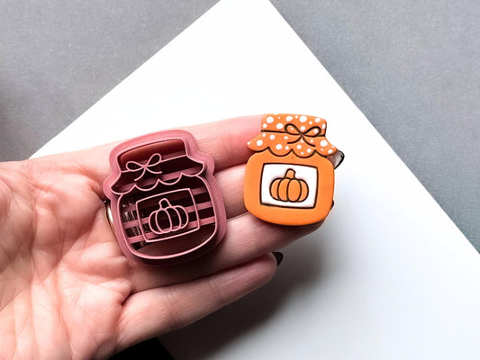 Halloween pumpkin jar polymer clay cutter and matching finished clay embellishment held in a hand for scale, featuring a pumpkin framed inside a striped jar with a decorative bow and polka-dot lid.