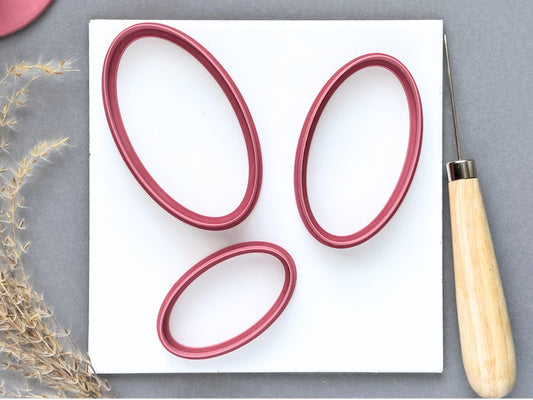 Three large oval polymer clay cutters displayed in different sizes and orientations on a white tile, featuring elongated oval shapes, smooth outlines and raised cutting walls.