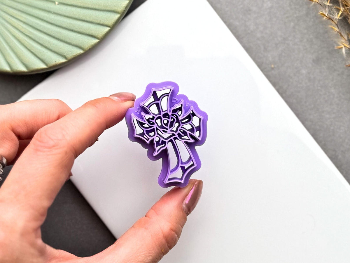Hand holding a stained glass cross with rose polymer clay cutter for size comparison, showing the intricate floral design and cutter details.