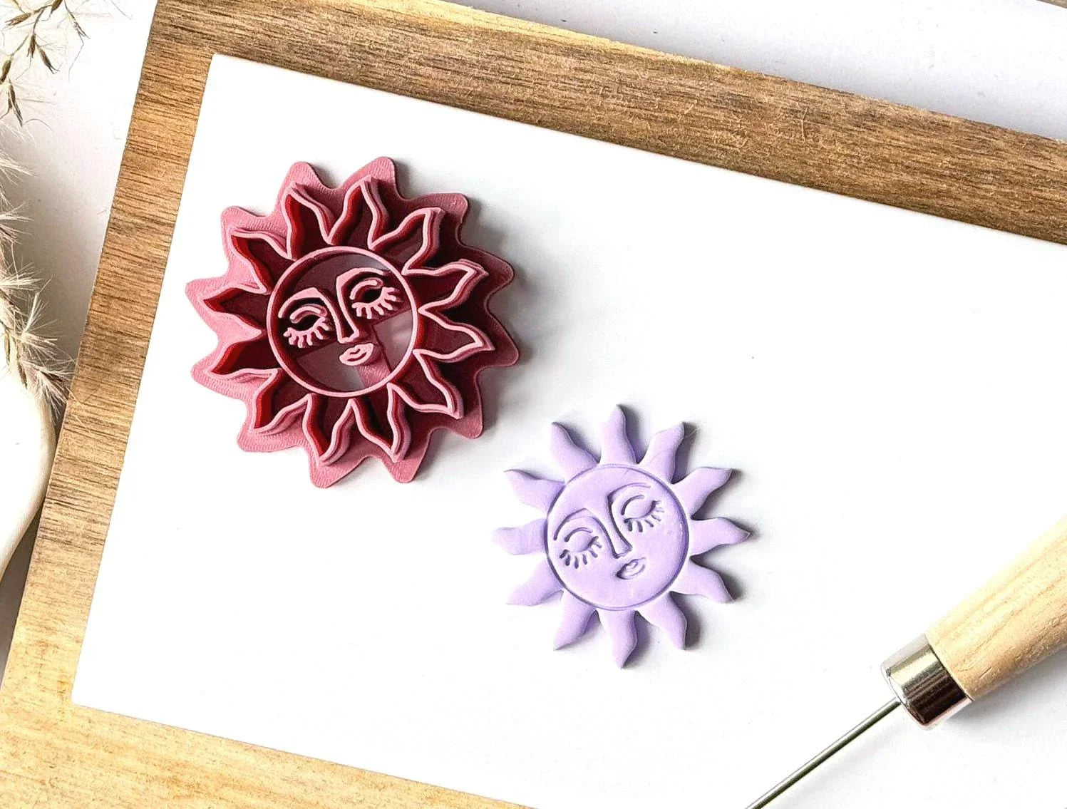 Pink celestial sun polymer clay cutter with matching lavender clay sun face cut-out displayed on a white ceramic tile.