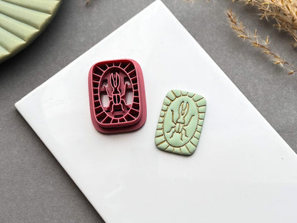 Beetle polymer clay cutter displayed beside a matching finished polymer clay embellishment featuring a simple beetle motif within a decorative segmented border.