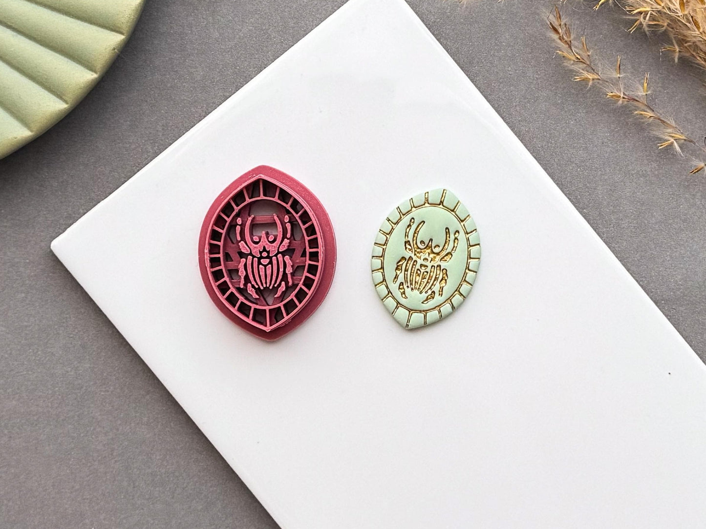 Goliath beetle polymer clay cutter displayed beside a matching finished polymer clay embellishment featuring a detailed Goliath beetle within a decorative geometric border.