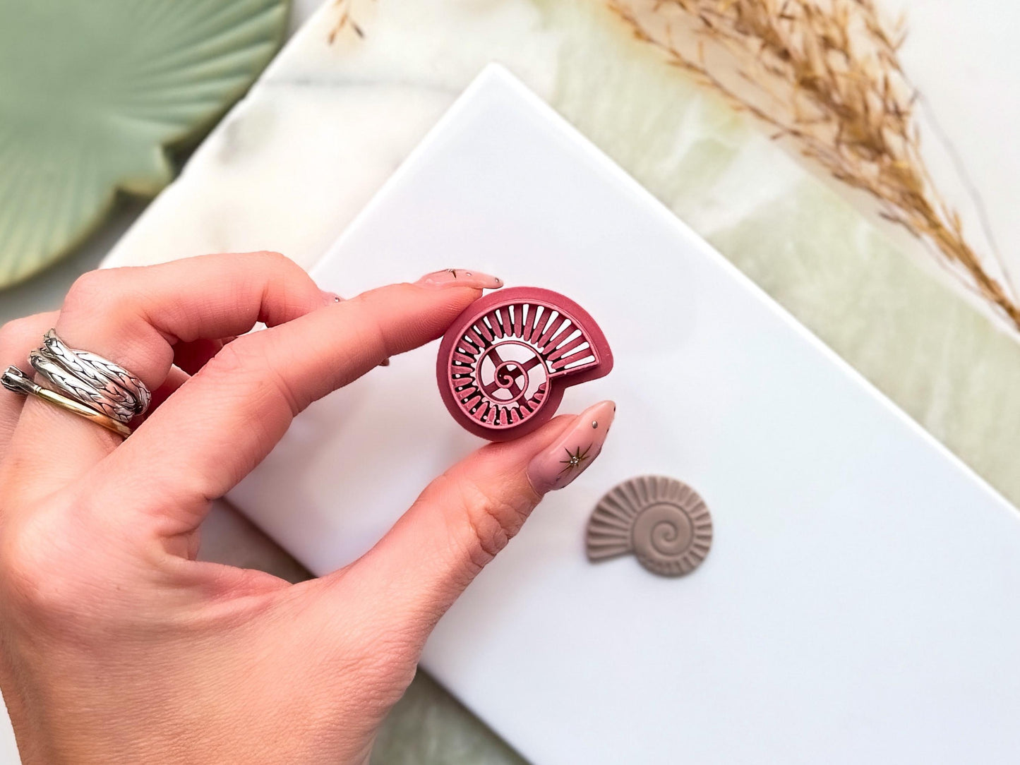 Overhead view of pink fossil seashell clay cutter showing the embossing lines support wall and air flow features to prevent polymer clay and fondant from sticking to the cutter.