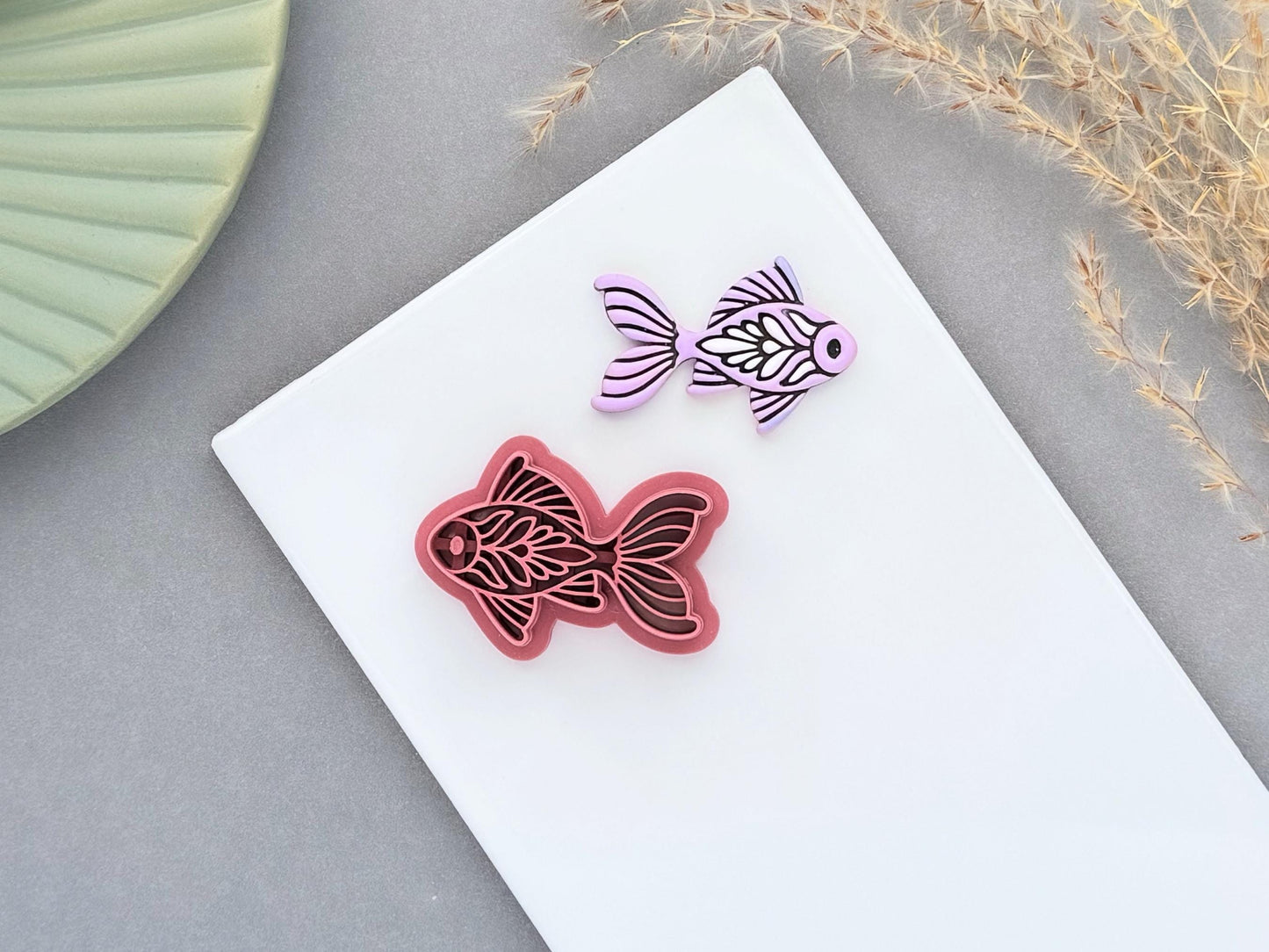 Decorative folk art style goldfish style polymer clay cutter with a lavender clay sample on a white ceramic tile background.