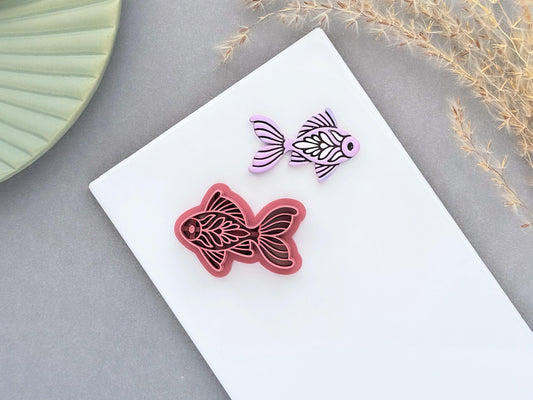 Decorative folk art style goldfish style polymer clay cutter with a lavender clay sample on a white ceramic tile background.