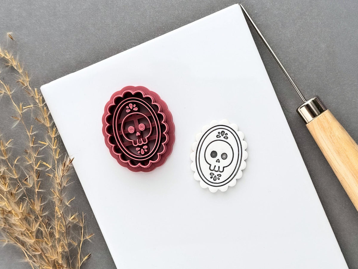 Gothic skull cameo polymer clay cutter displayed beside a matching finished clay cut-out, featuring a skull with decorative floral details inside an ornate scalloped oval frame.