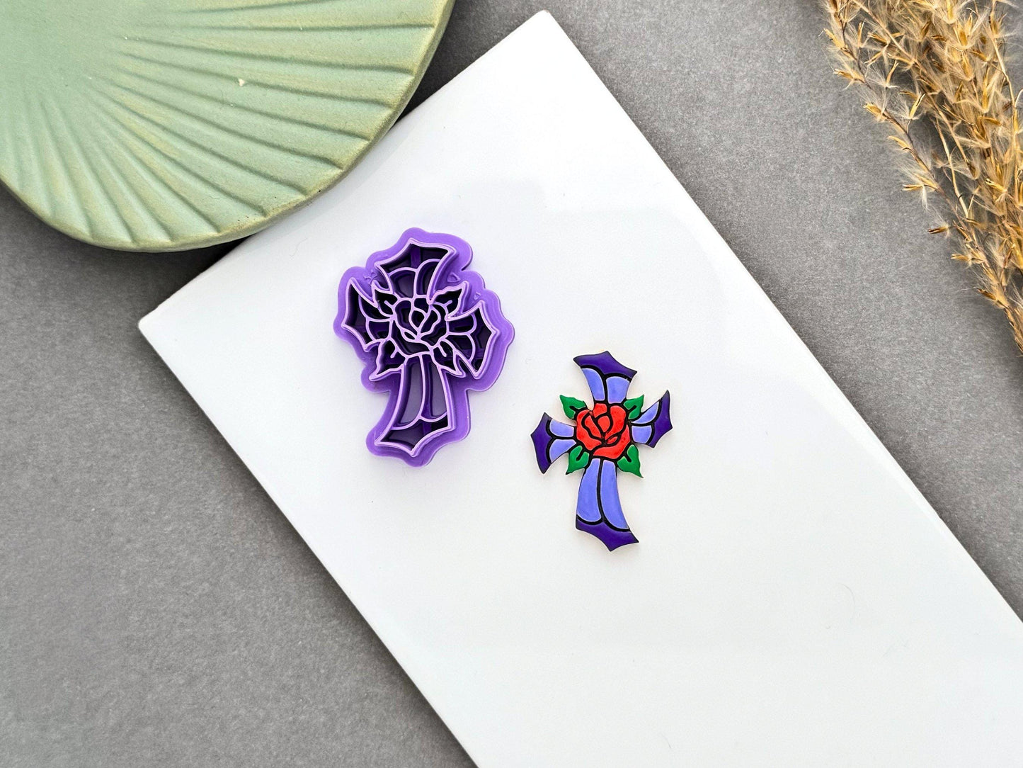Purple stained glass cross polymer clay cutter with a rose design beside a finished stained glass style cross clay embellishment.