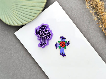 Purple stained glass cross polymer clay cutter with a rose design beside a finished stained glass style cross clay embellishment.