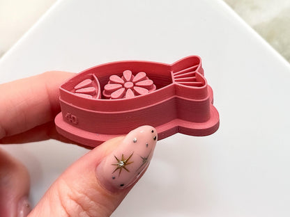 Close up image of the floral fish clay cutter being held in a hand. The picture clearly shows the stamp detail and sharp cutting edge.