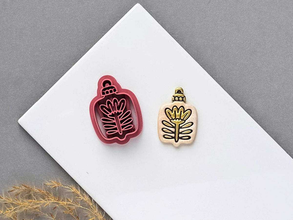 Botanical Christmas bauble polymer clay cutter featuring a stylised flower with a long stem and decorative leaves, displayed beside a matching finished clay embellishment.