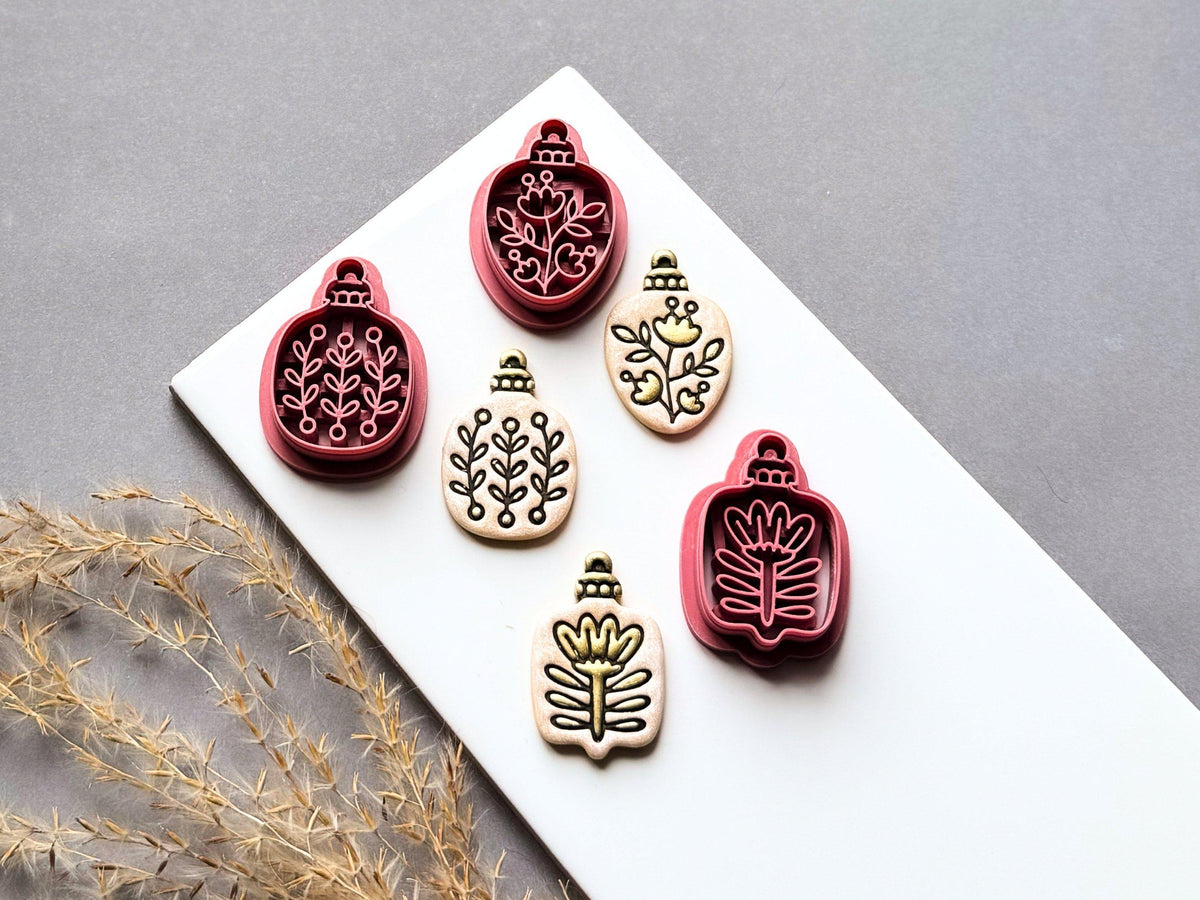 Set of four botanical Christmas bauble polymer clay cutters featuring folk art floral and leafy designs, displayed alongside matching finished clay embellishments.