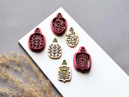 Set of four botanical Christmas bauble polymer clay cutters featuring folk art floral and leafy designs, displayed alongside matching finished clay embellishments.