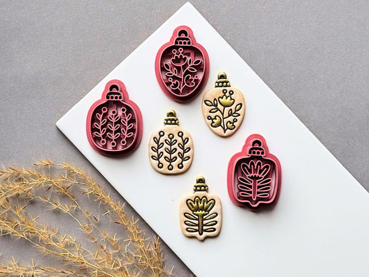 Christmas botanical bauble polymer clay cutters displayed in three designs beside matching finished clay cut-outs, featuring delicate folk art floral and leafy patterns within decorative bauble shapes.