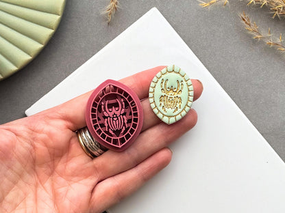 Goliath beetle polymer clay cutter and matching finished polymer clay embellishment held in a hand for scale, featuring a detailed Goliath beetle within a decorative geometric border.