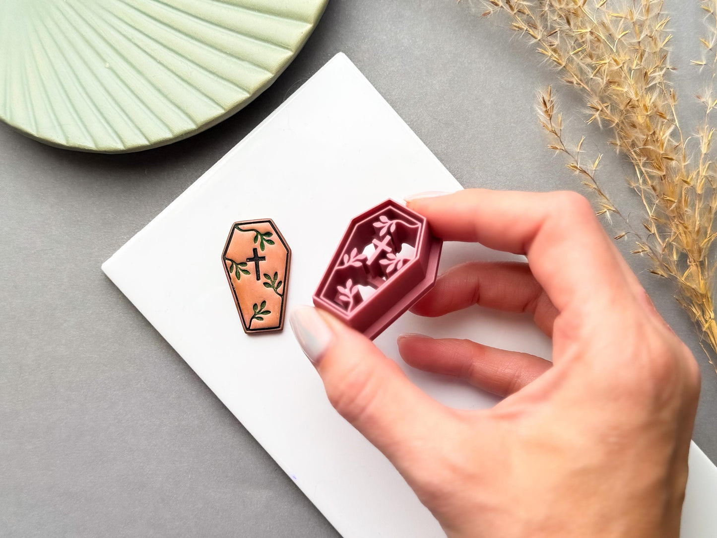 Coffin-shaped polymer clay cutter held in a hand, shown beside a matching finished clay embellishment featuring a cross and delicate botanical details, perfect for gothic, Halloween, alternative and dark botanical clay projects.