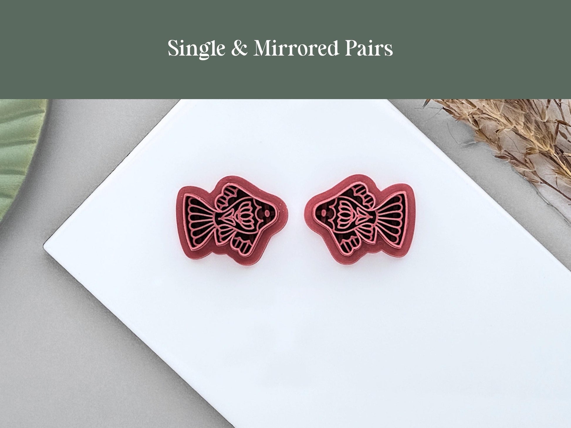 Single and mirrored pair ornamental fish polymer clay cutters displayed side by side on a white ceramic tile. The folk art-inspired fish designs are shown in left and right-facing versions for creating matching jewellery pieces.