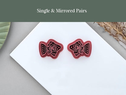 Single and mirrored pair ornamental fish polymer clay cutters displayed side by side on a white ceramic tile. The folk art-inspired fish designs are shown in left and right-facing versions for creating matching jewellery pieces.